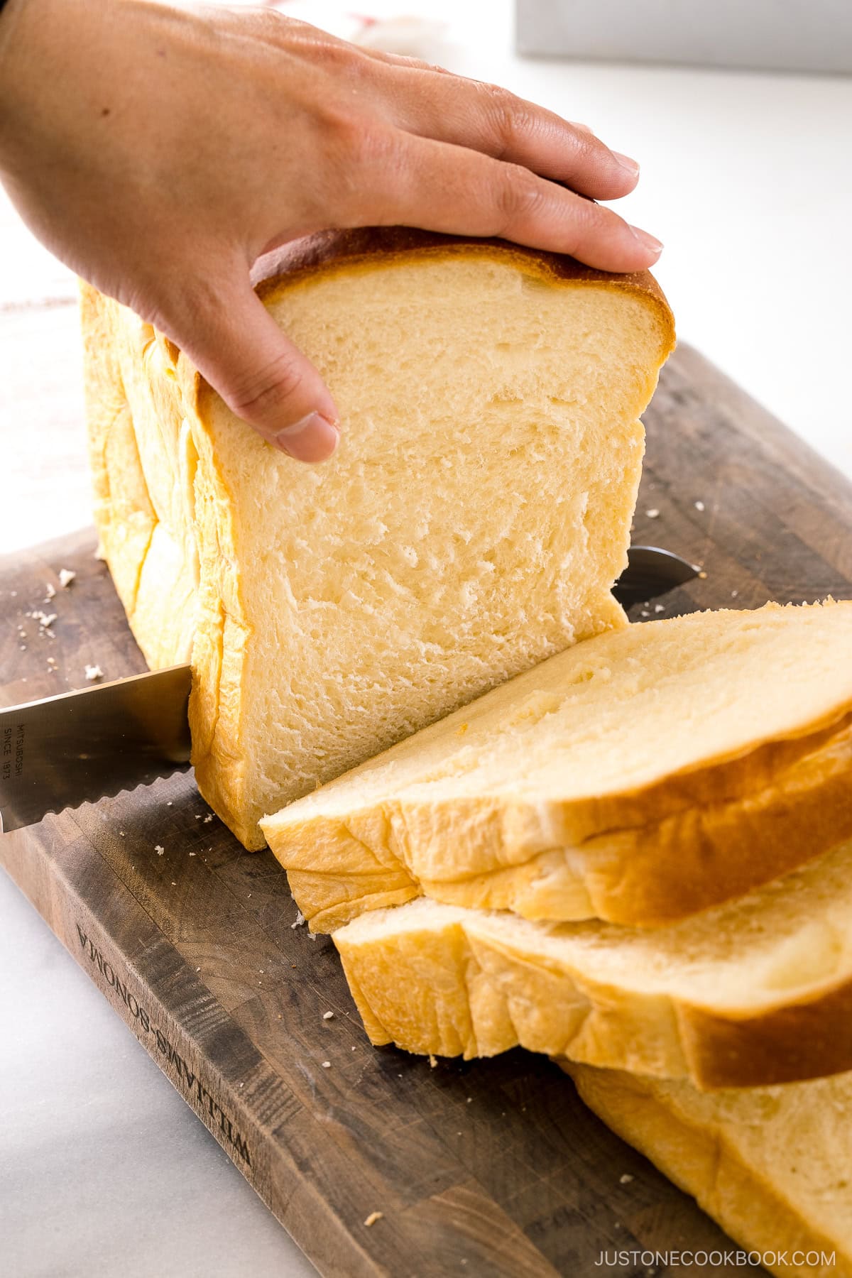A loaf of Japanese milk bread (shokupan) being sliced with a sharp bread knife.